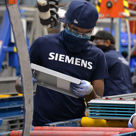 Seimens apprentice wearing dark blue Seimens shirt, mask and safety glasses inspecting a piece of material